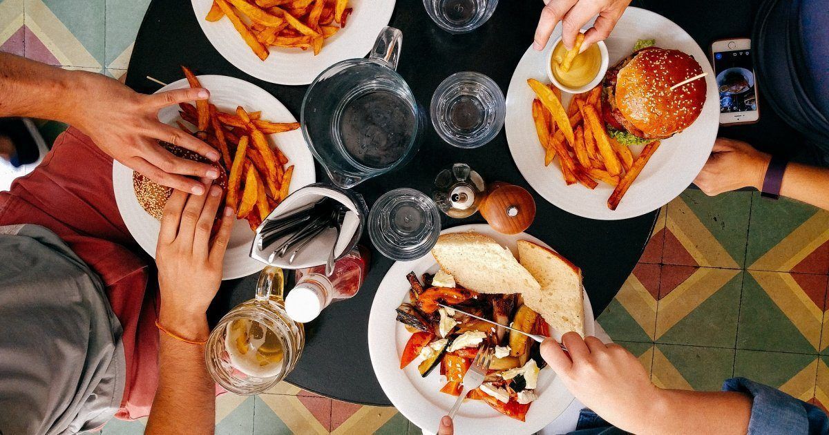 People at a table sharing a meal: burgers, fries, and vegetables.