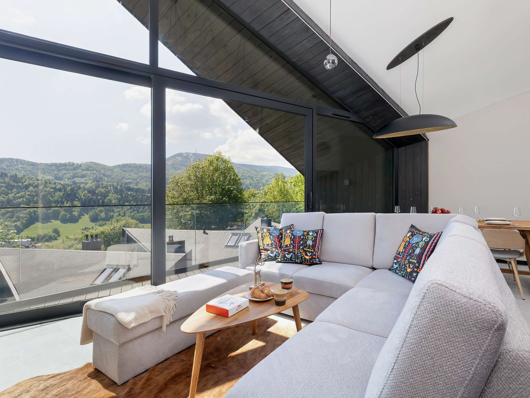 Modern living room with gray sectional, coffee table, and large windows overlooking a scenic hillside.