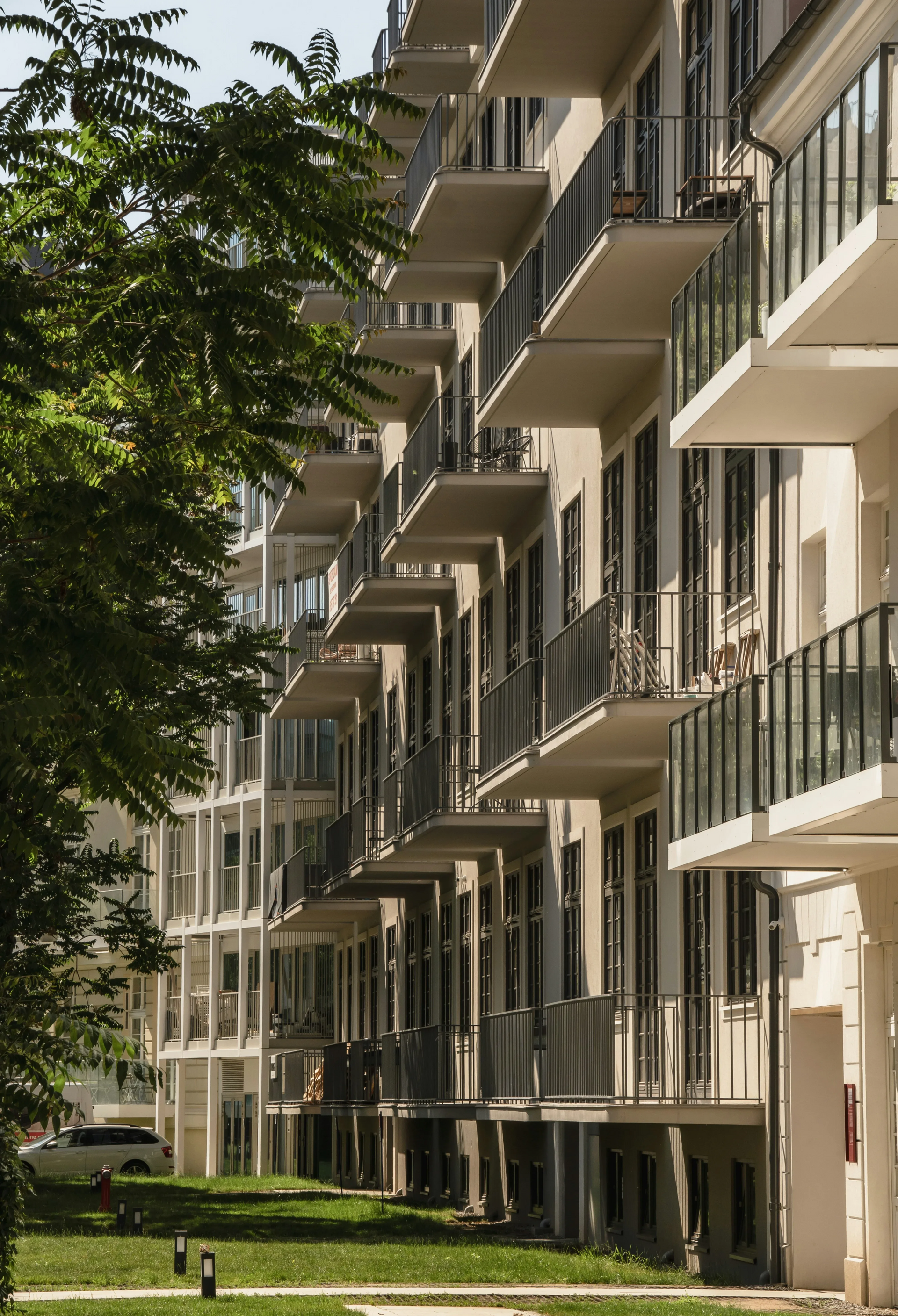 Mehrstöckiges Wohnhaus mit Balkonen, Bäumen und Grünflächen.