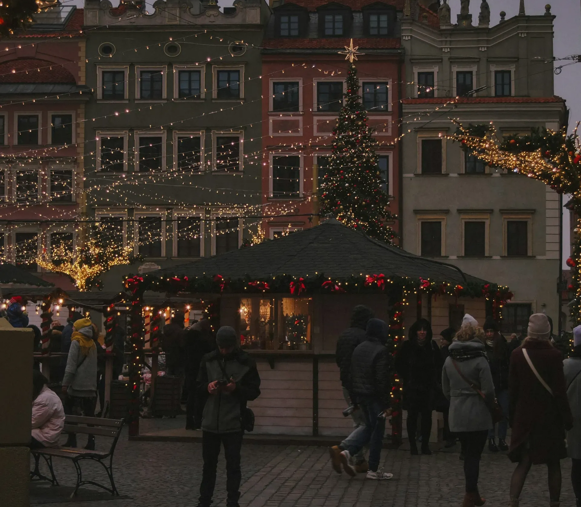 Jarmark bożonarodzeniowy W Warszawie o zmierzchu: stragany, światła i choinka.