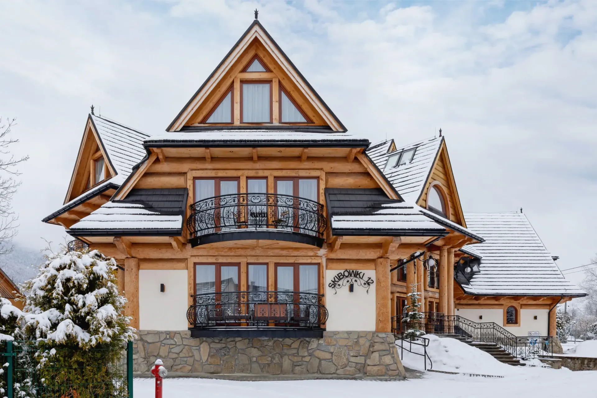 Drewniany dom w stylu domku myśliwskiego z ośnieżonym dachem i otoczeniem, balkonem z ozdobną balustradą.