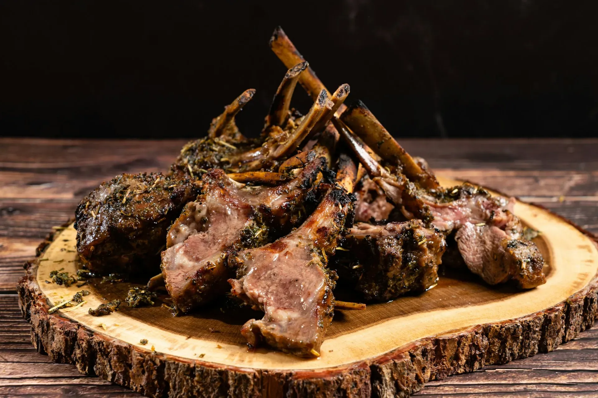 Roasted lamb chops on a wooden platter with dark background.