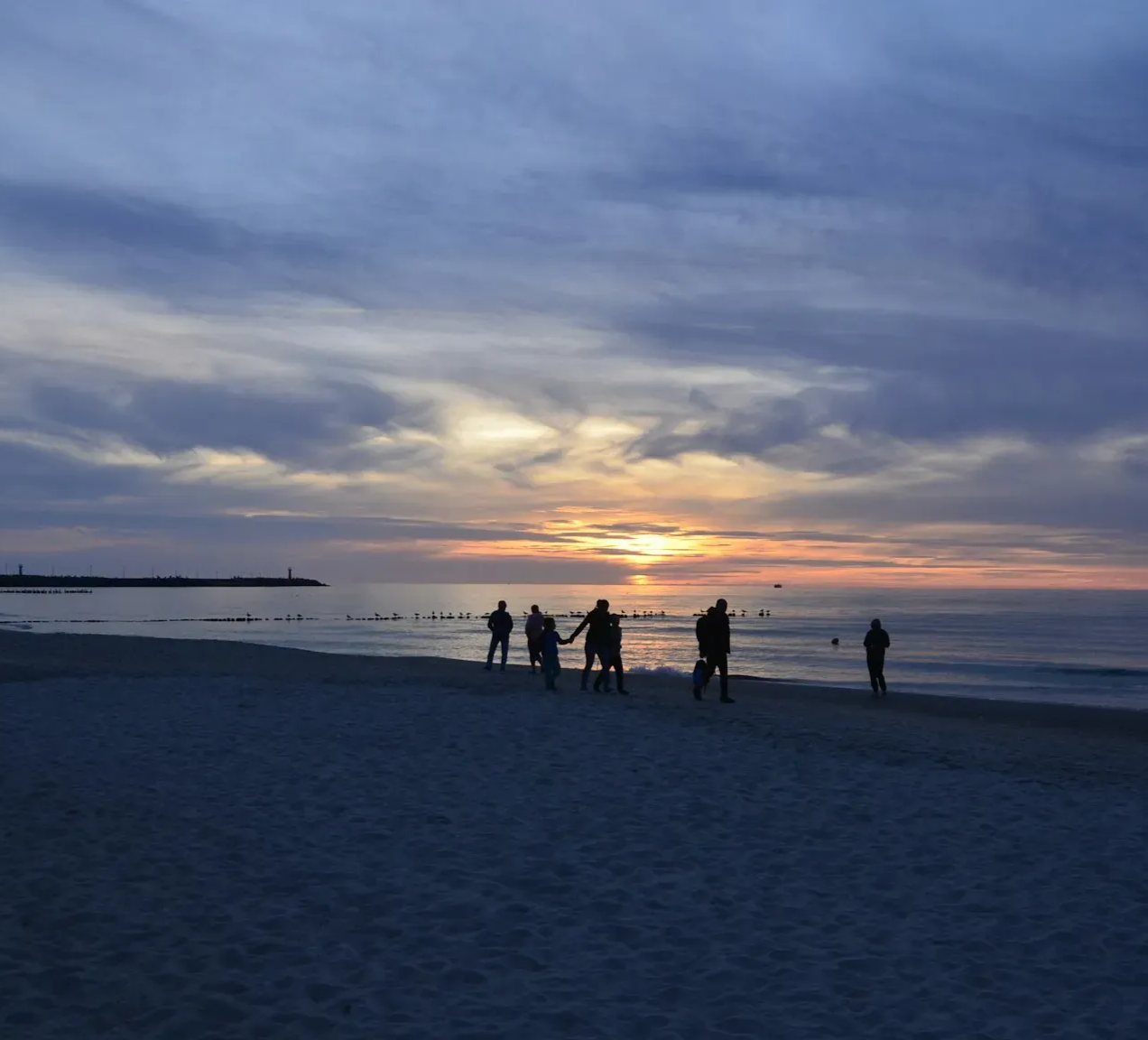 Plaża o zmierzchu, sylwetki ludzi, zachód słońca nad wodą.