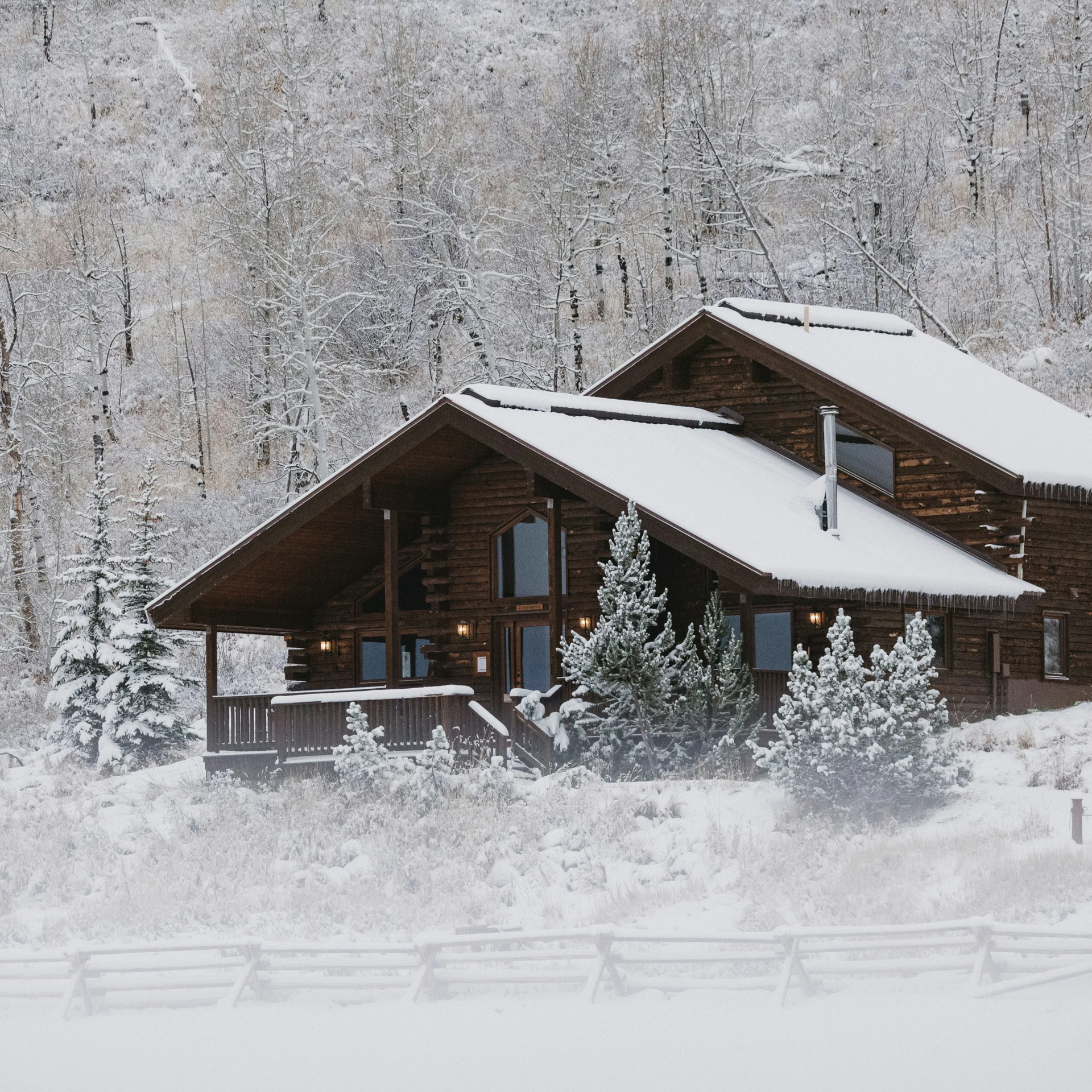 Wooden cabin covered in snow in a snowy forest.