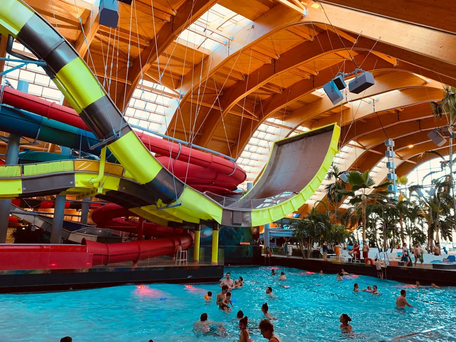 Indoor water park with multiple waterslides and a wave pool, people swimming.