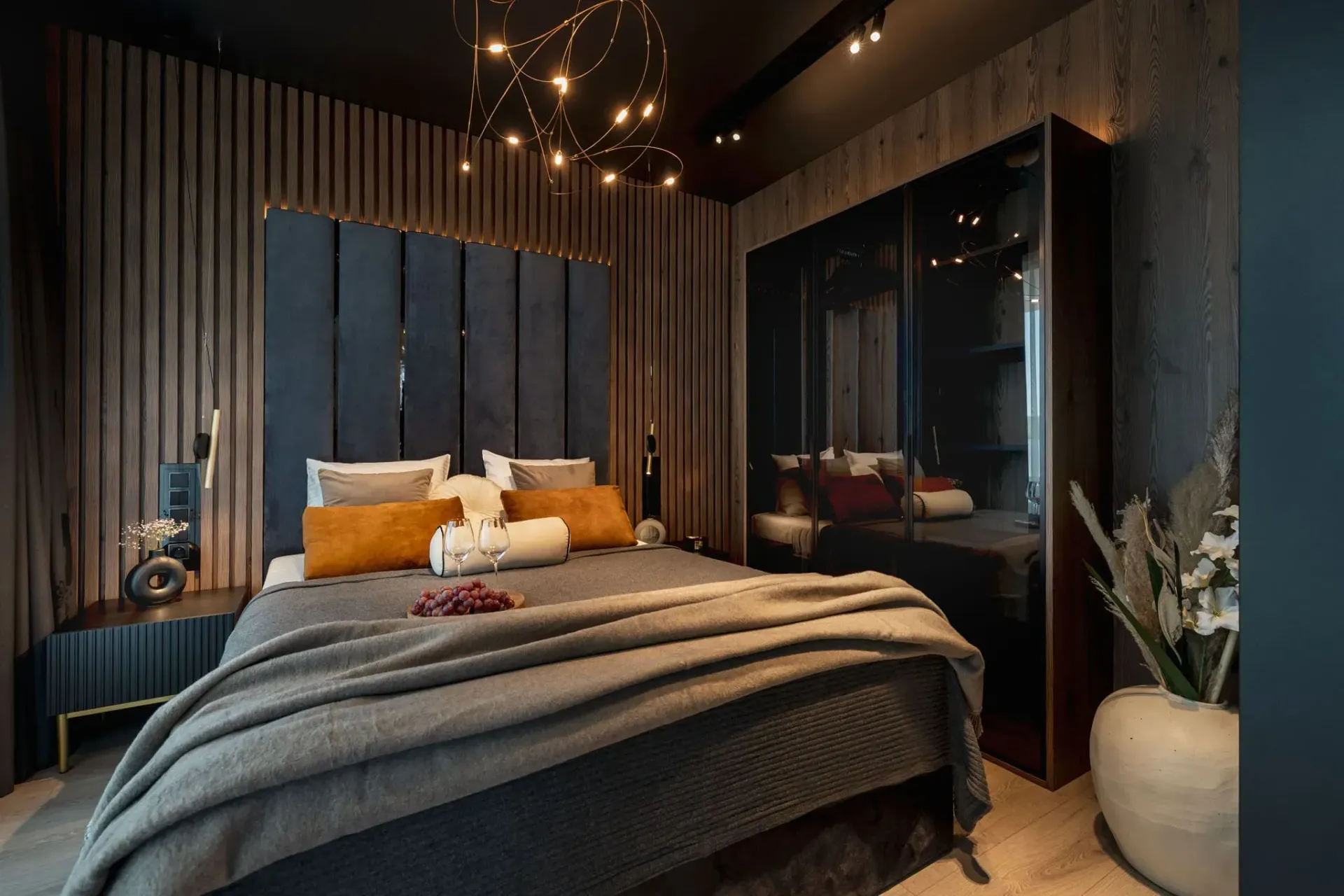 Bedroom with blue upholstered headboard, wood paneling, dark wardrobe, and decorative lighting.