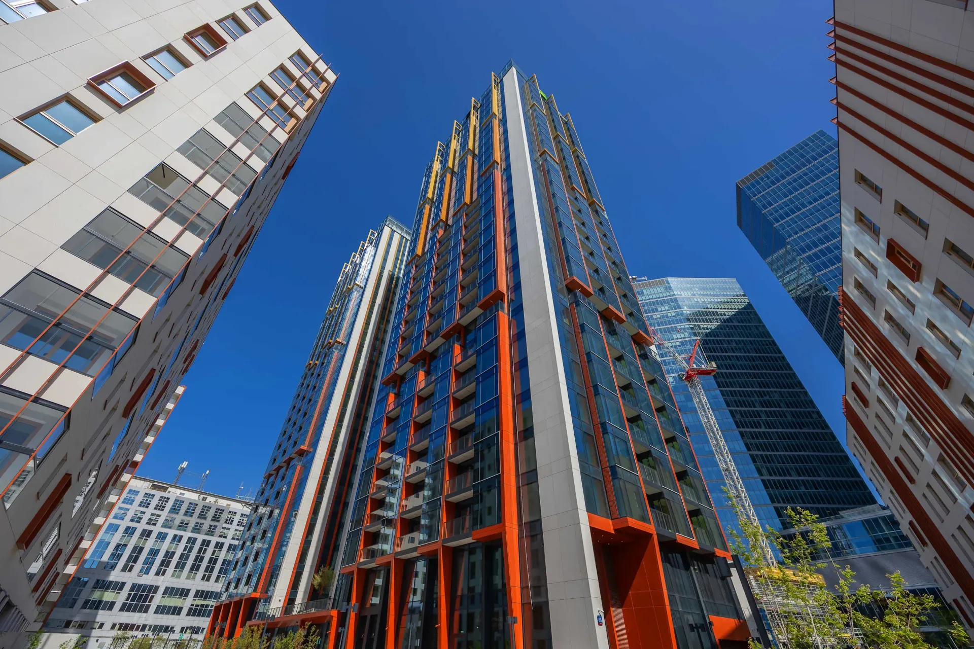 Wysokie, nowoczesne budynki na tle czystego, błękitnego nieba, ze szklanymi i pomarańczowymi akcentami na fasadach.