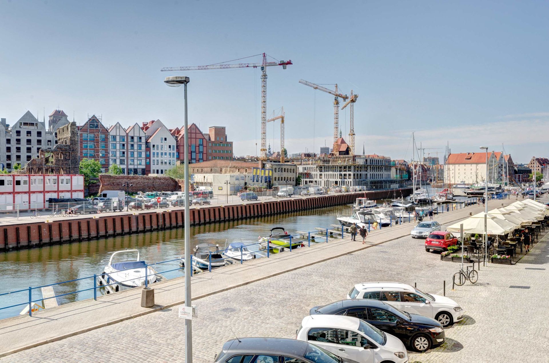 Widok na nabrzeże z łodziami, samochodami, dźwigami budowlanymi i kolorowymi budynkami w Gdańsku, w Polsce.