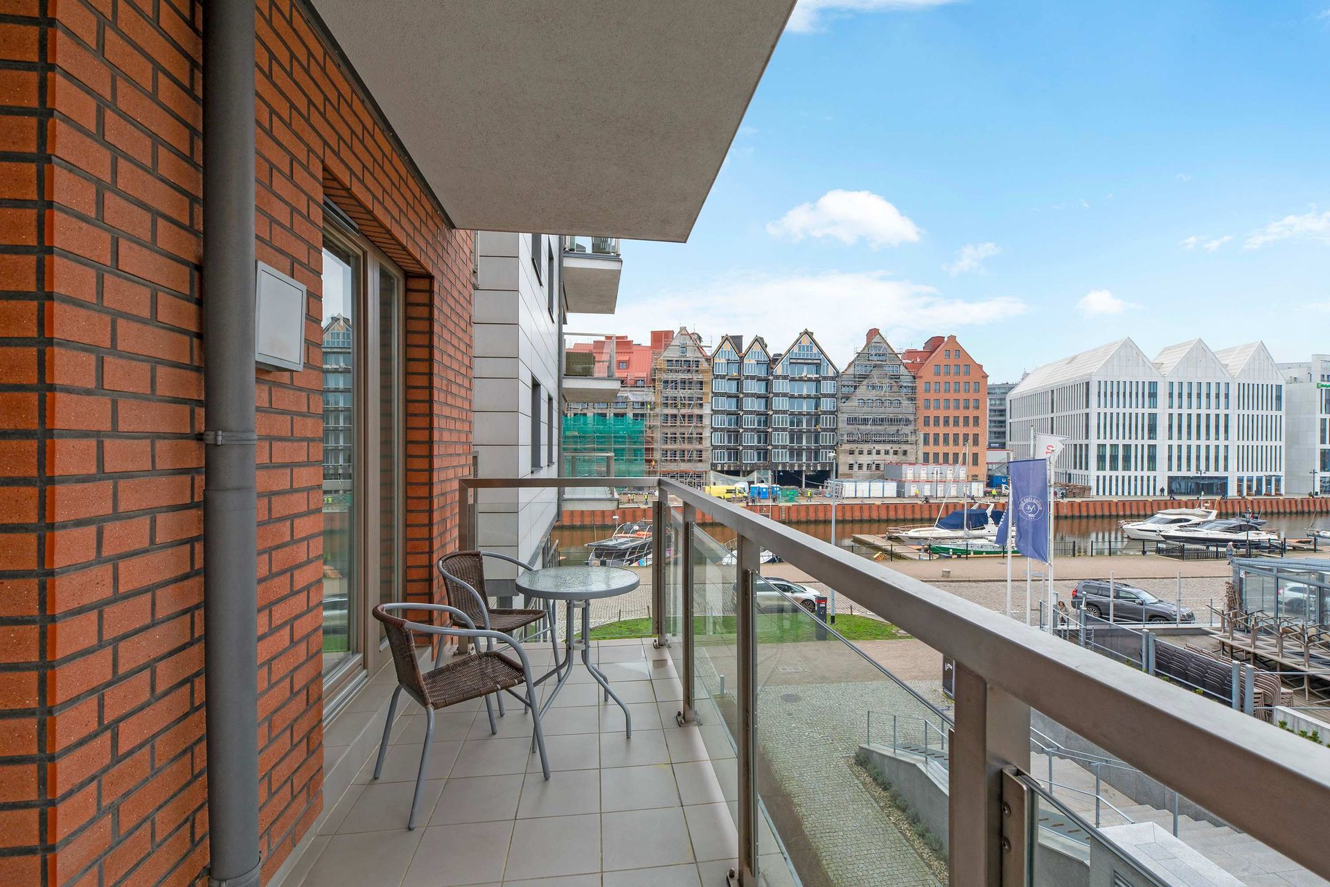 Widok z balkonu na port, ceglany budynek, stół, krzesła i kolorowe budynki w oddali.