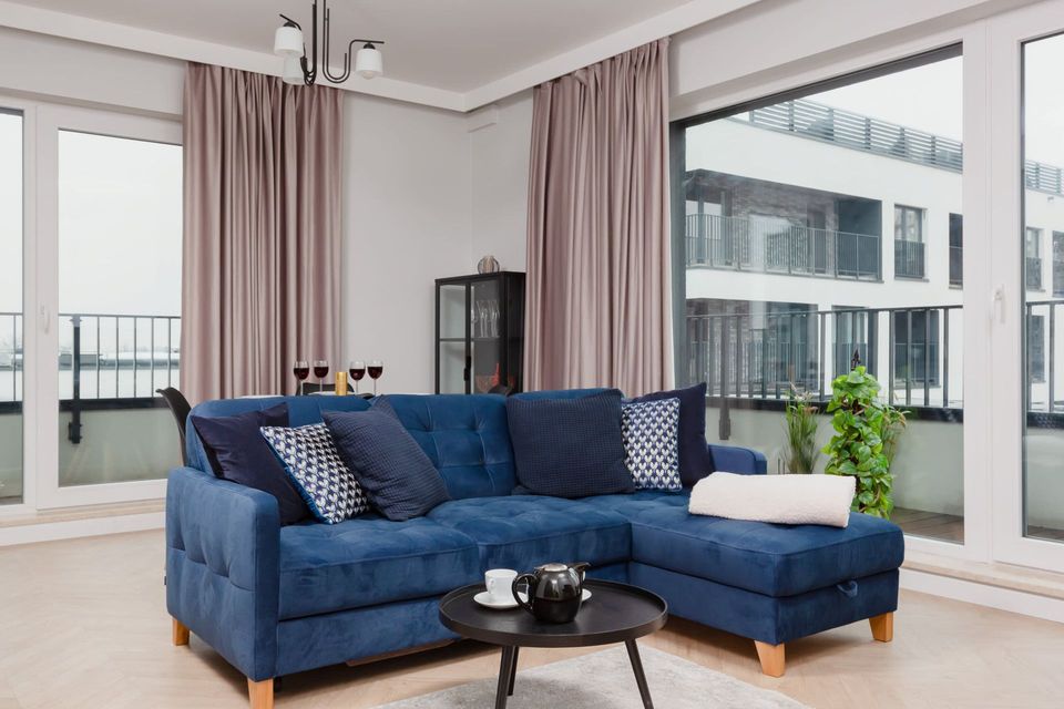 Niebieska sofa modułowa w jasnym salonie z dużymi oknami i małym stolikiem kawowym