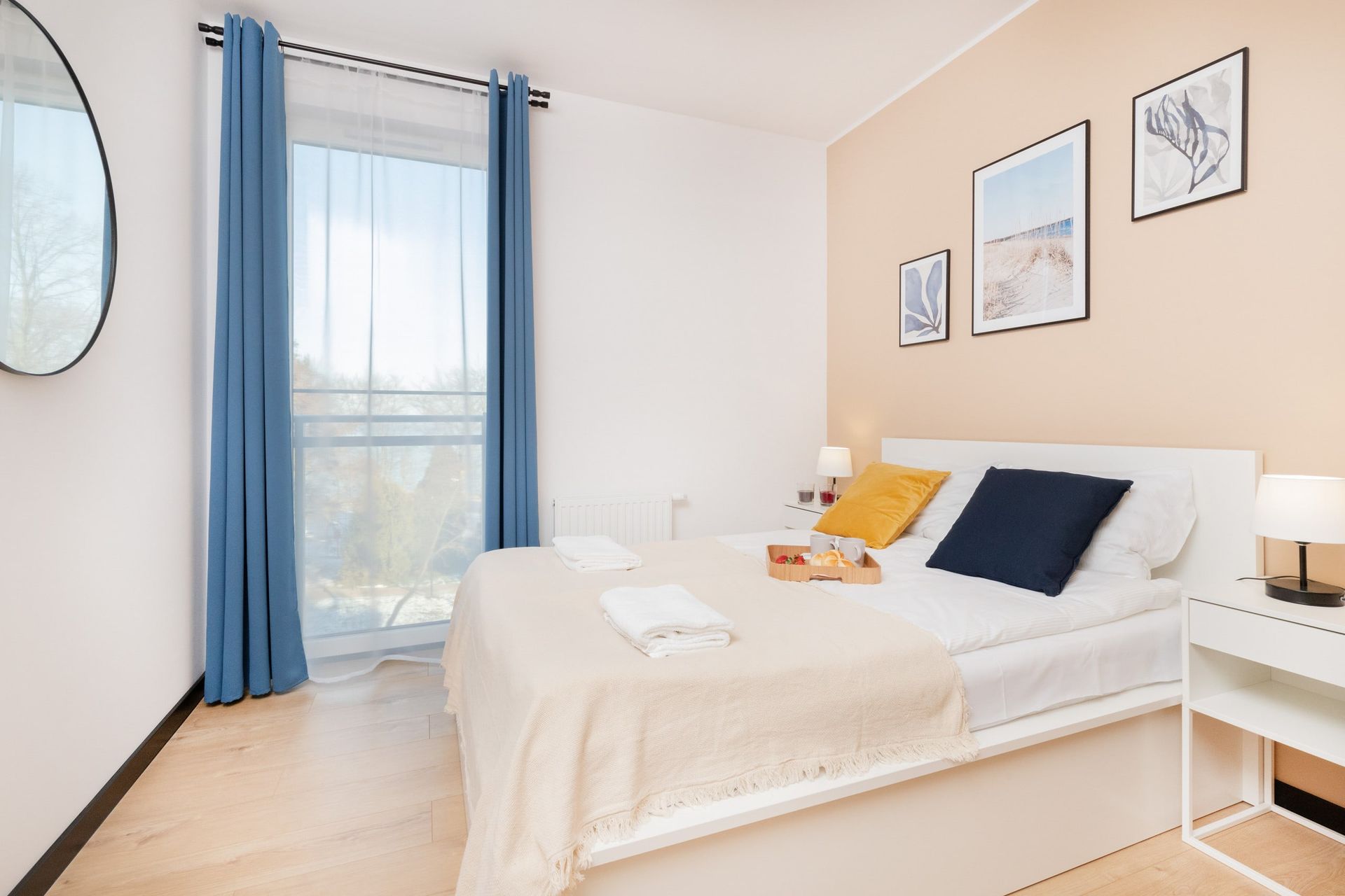 Sypialnia z łóżkiem, niebieskimi zasłonami, dziełami sztuki i okrągłym lustrem.