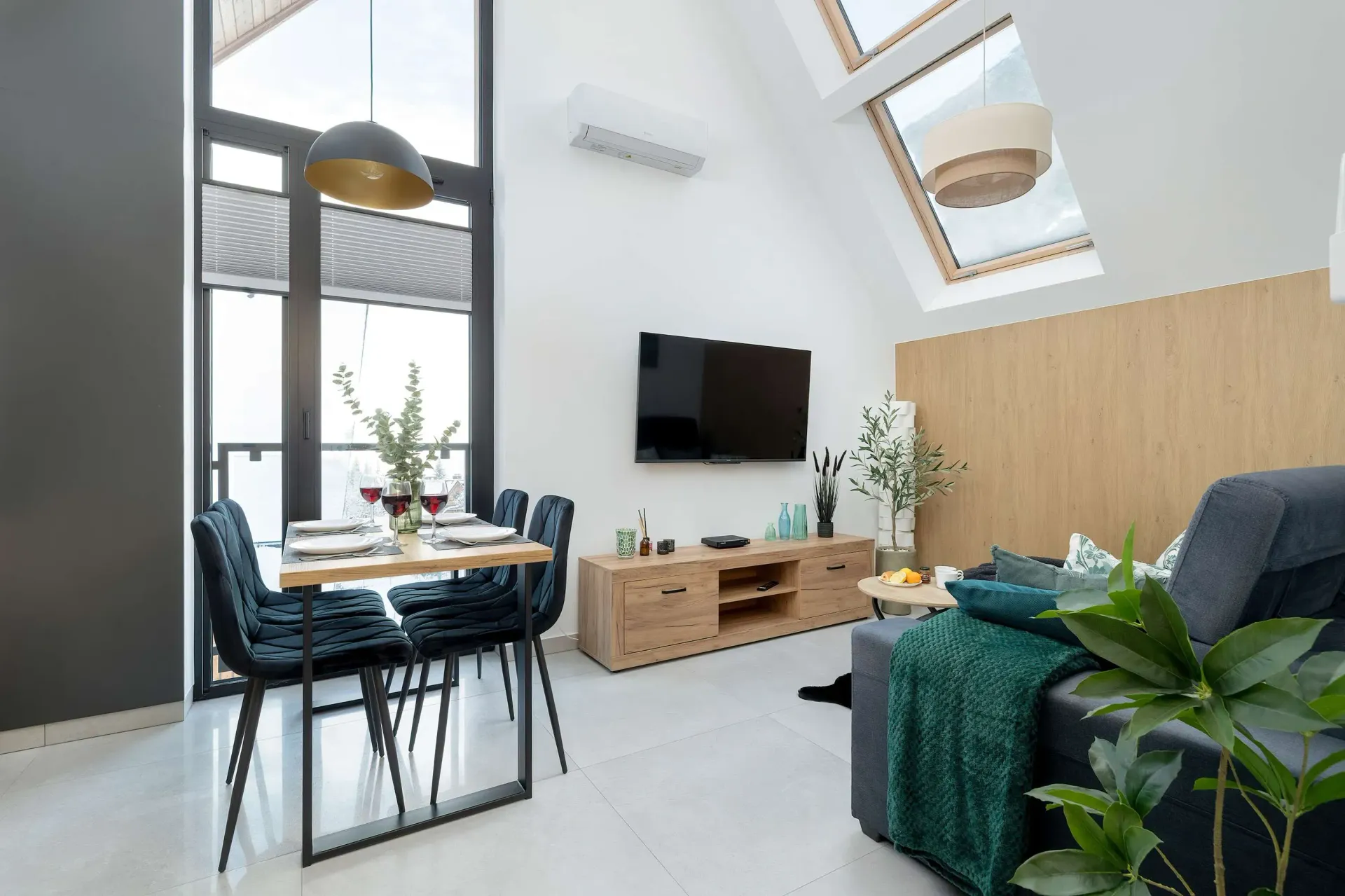 Salon ze stołem jadalnym, sofą, telewizorem i oknem dachowym w nowoczesnym domu z białymi ścianami i akcentami drewnianymi.
