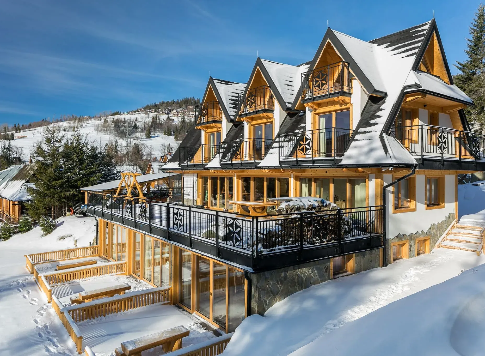 Zaśnieżony domek z drewnianą fasadą i dwuspadowym dachem, położony na zboczu wzgórza.