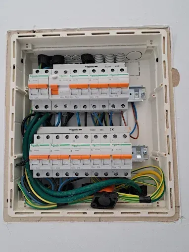 Panel de interruptores eléctricos con filas de disyuntores y cables agrupados dentro de un gabinete blanco.