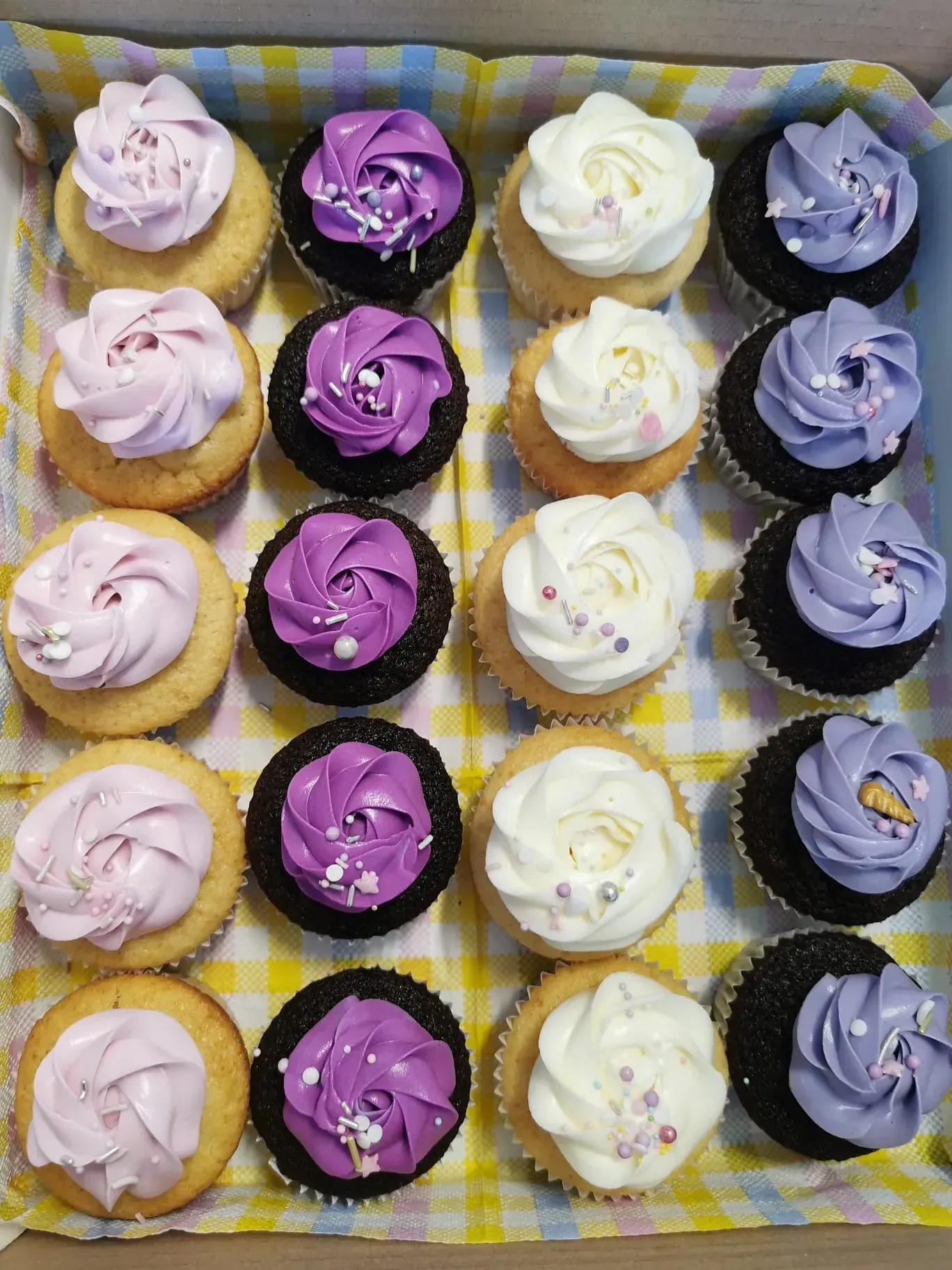 Una caja de cupcakes con glaseado morado y blanco y chispas.