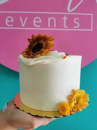 Una persona sostiene un pastel con un girasol encima.