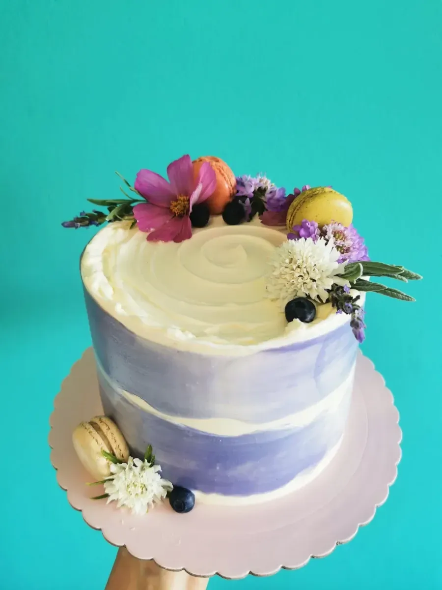 Una persona sostiene un pastel morado con flores y macarons encima.