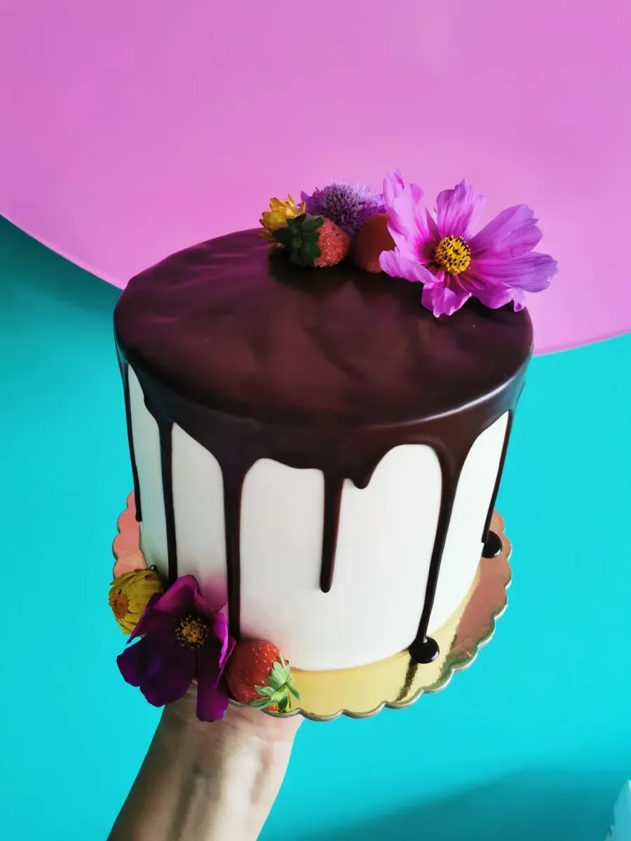 Una persona sostiene un pastel de chocolate con flores encima.