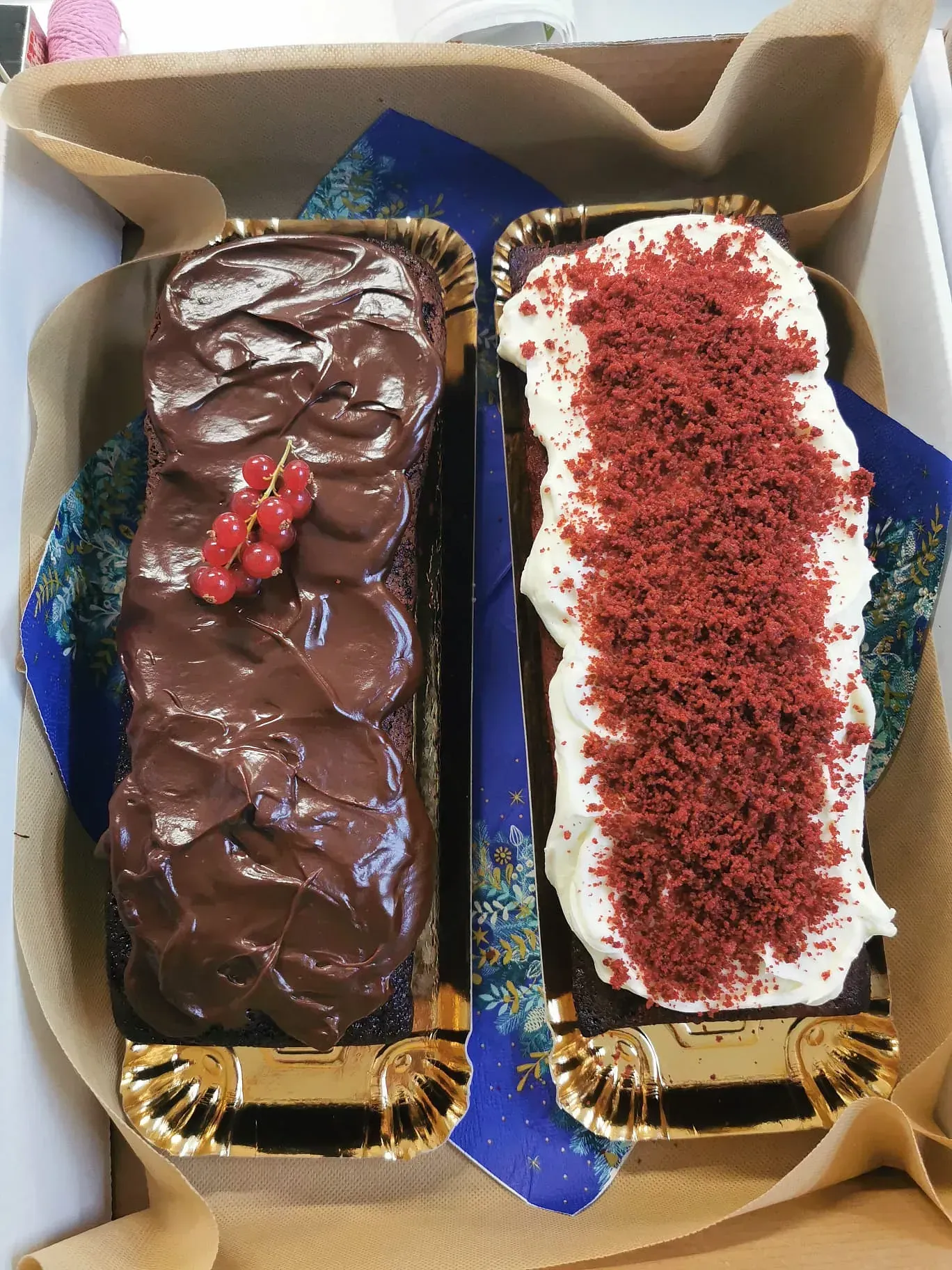 Dos pasteles en una caja, uno de chocolate y otro de terciopelo rojo.
