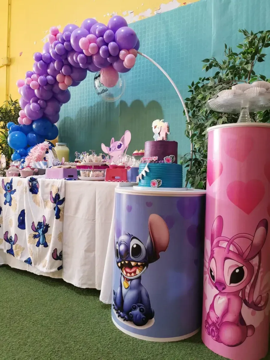Una mesa con un arco de globos morados y pilares rosas con puntadas y un ángel en ellos.