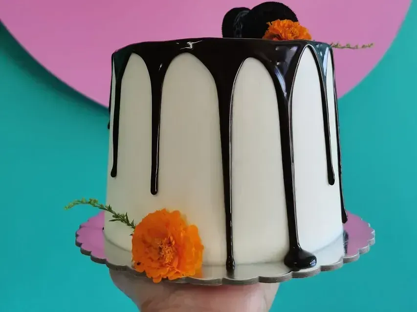 Una persona sostiene un pastel blanco con chocolate goteando.