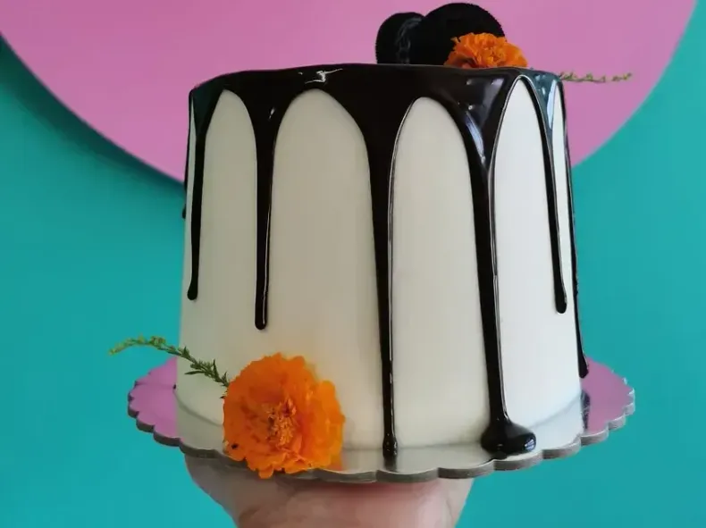 Una persona sostiene un pastel blanco con chocolate goteando.