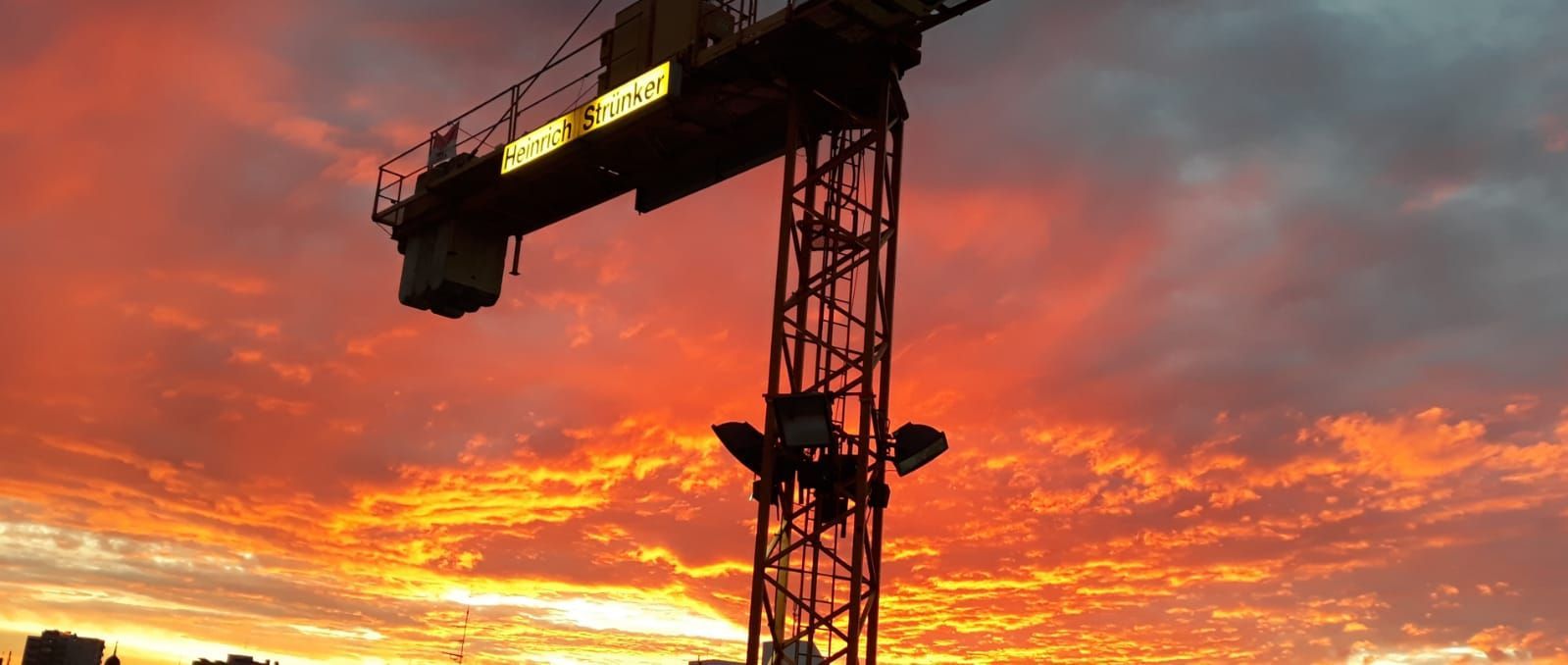 Die Silhouette eines Baukrans zeichnet sich vor dem Abendhimmel ab.