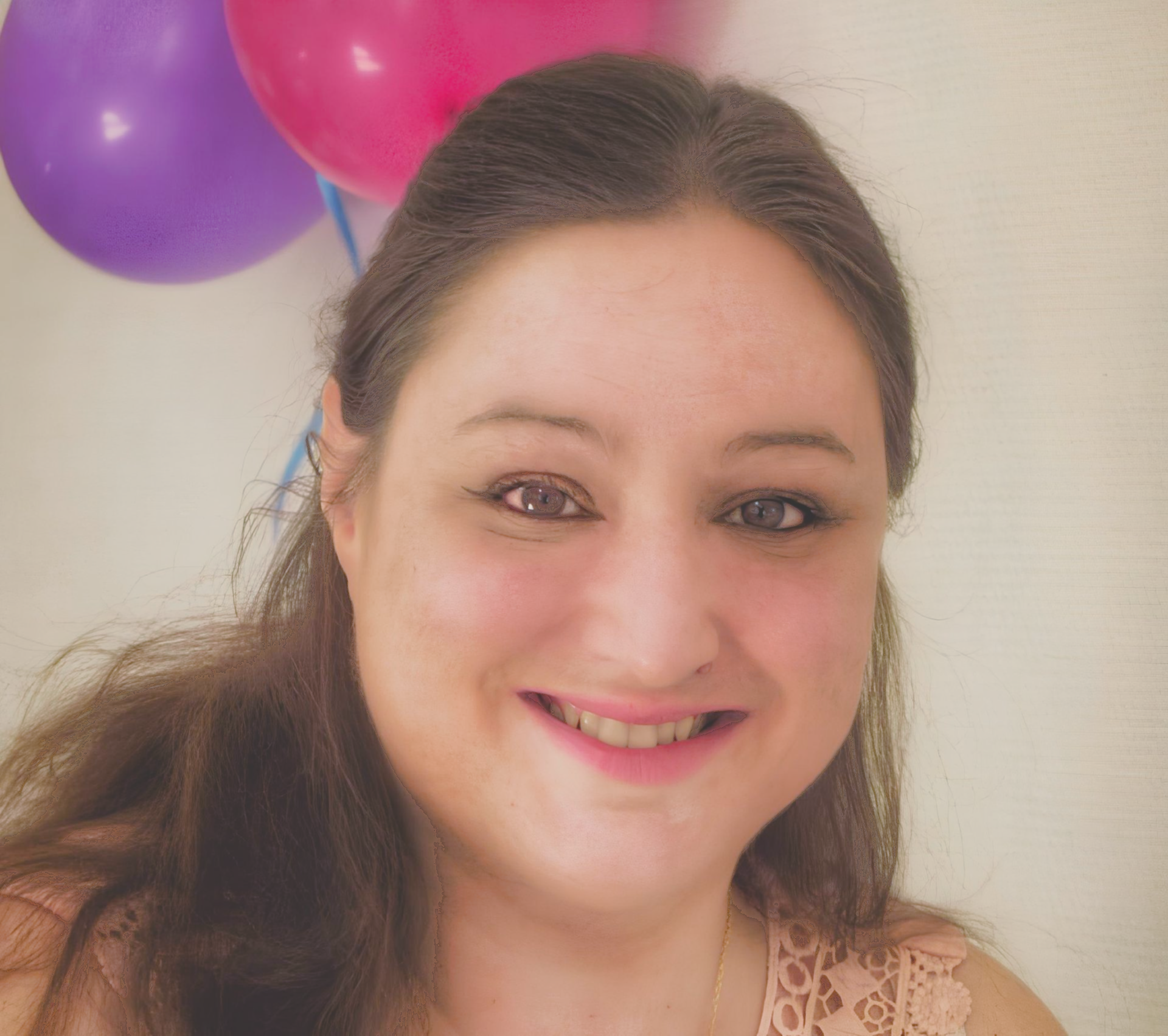 Femme souriante, vêtue d'un haut en dentelle rose, avec des ballons violets et roses en arrière-plan.