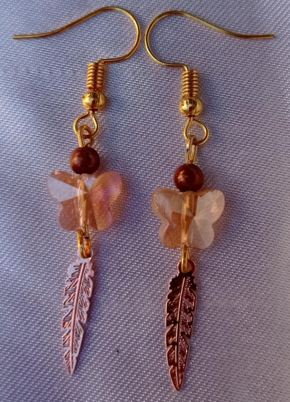 Boucles d'oreilles dorées : cristal en forme de papillon, perle brune et breloque en forme de plume.