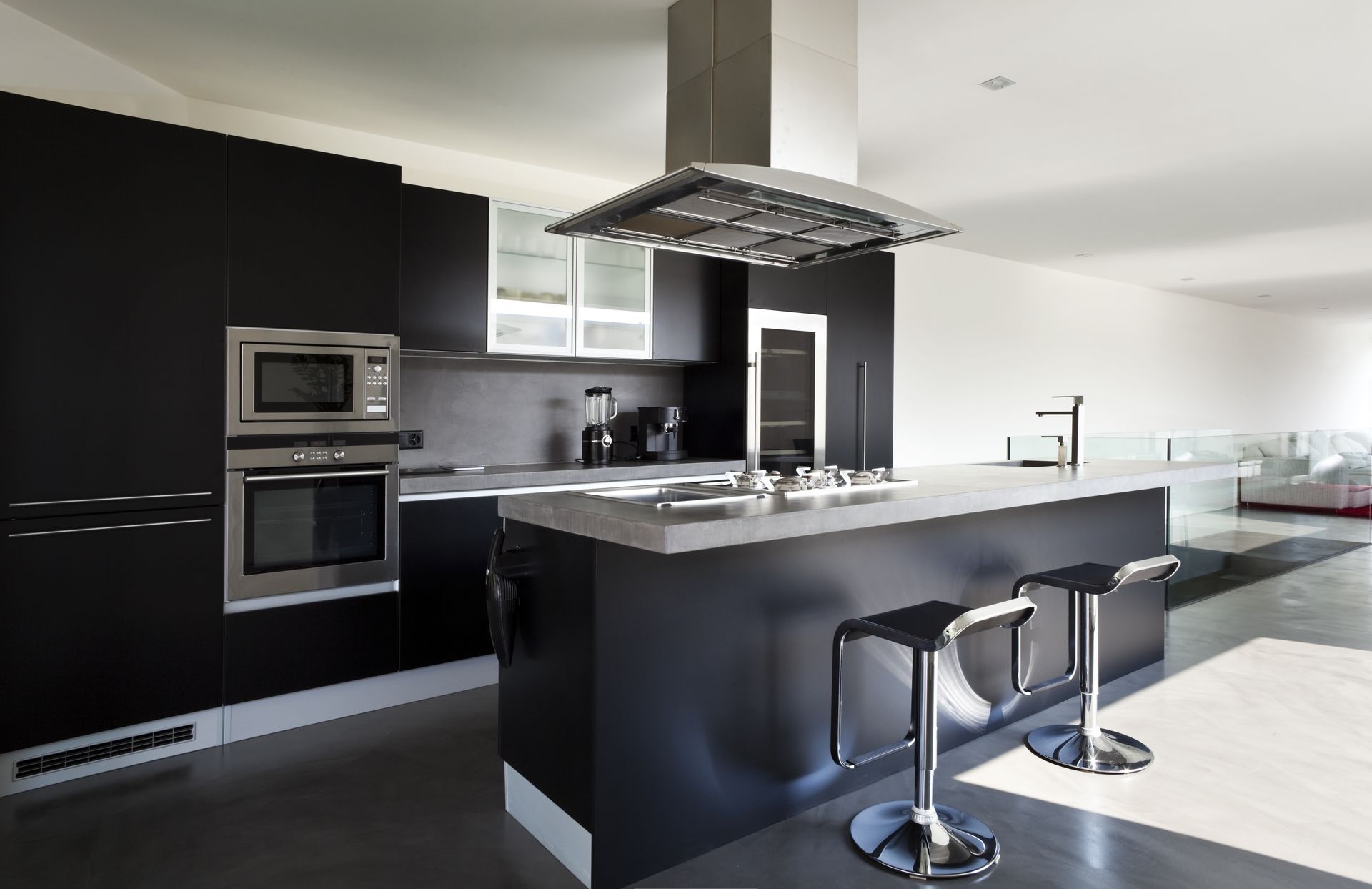 Cocina moderna de color negro con isla, dos taburetes de bar, electrodomésticos de acero inoxidable y campana extractora.