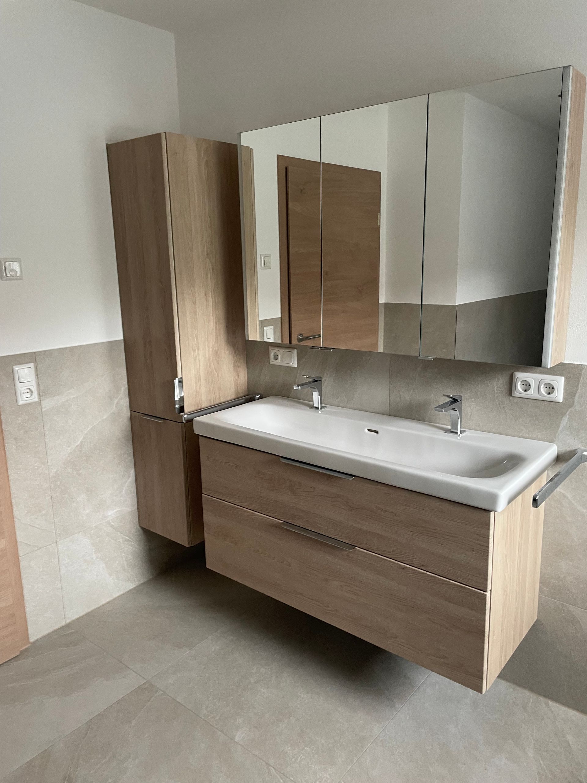 Moderner Badezimmerschrank mit Holzschränken, Spiegel, weißem Waschbecken und beigefarbenen Fliesenwänden