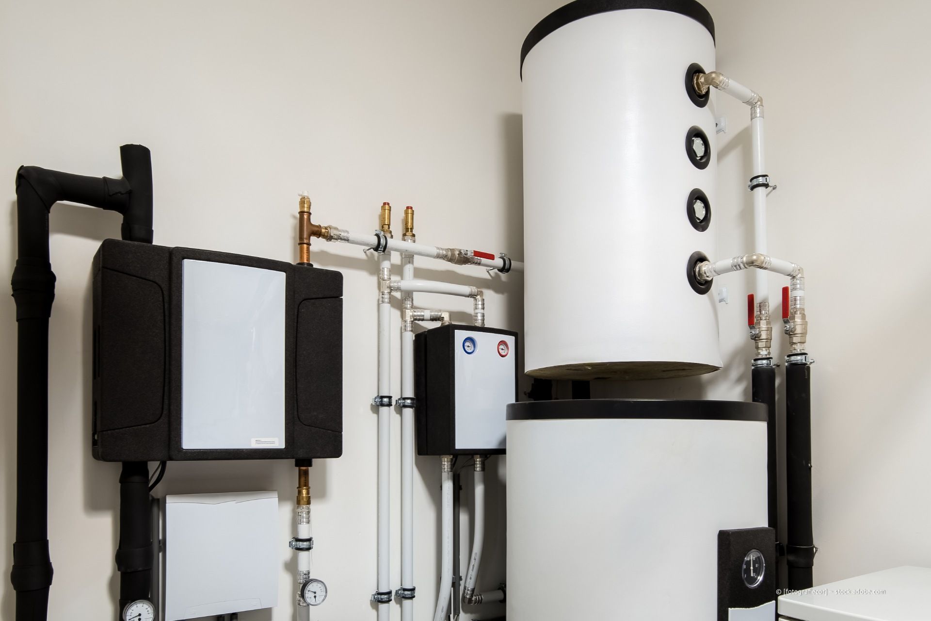 Industriekessel und Rohrleitungssystem mit weißen Tanks und schwarzen Anlagenteilen an einer Wand