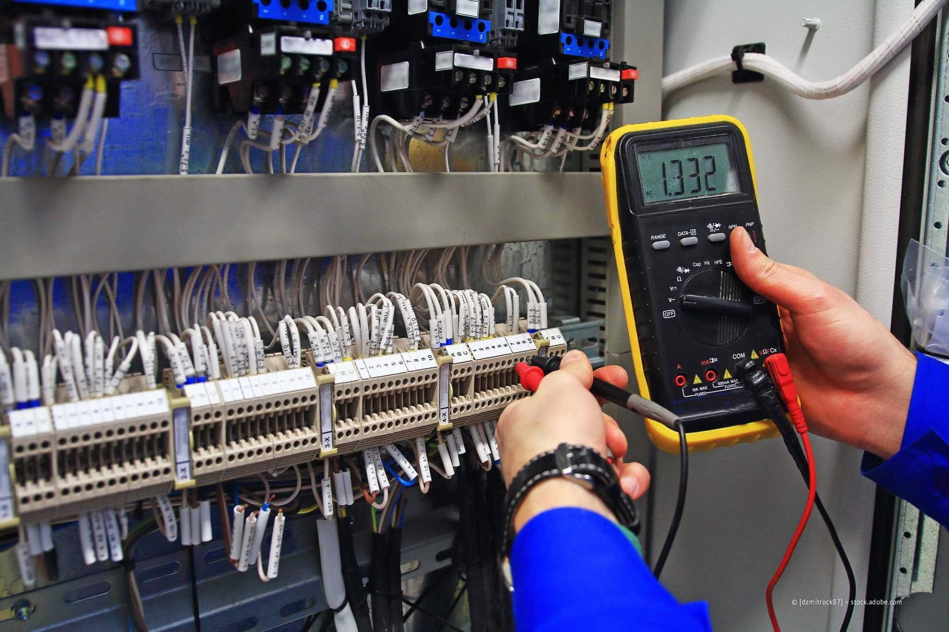Techniker prüft mit einem Multimeter die Verkabelung in einem elektrischen Schaltschrank.