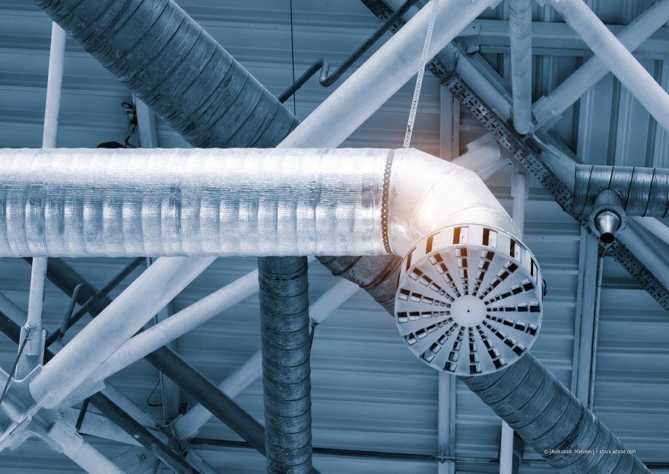 Silberne Lüftungsrohre und Deckenventilatoren in einem Industrieinterieur, von unten betrachtet.