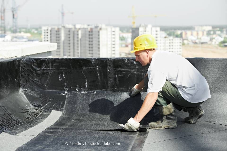 Ein Mann mit Schutzhelm arbeitet auf einem Dach.