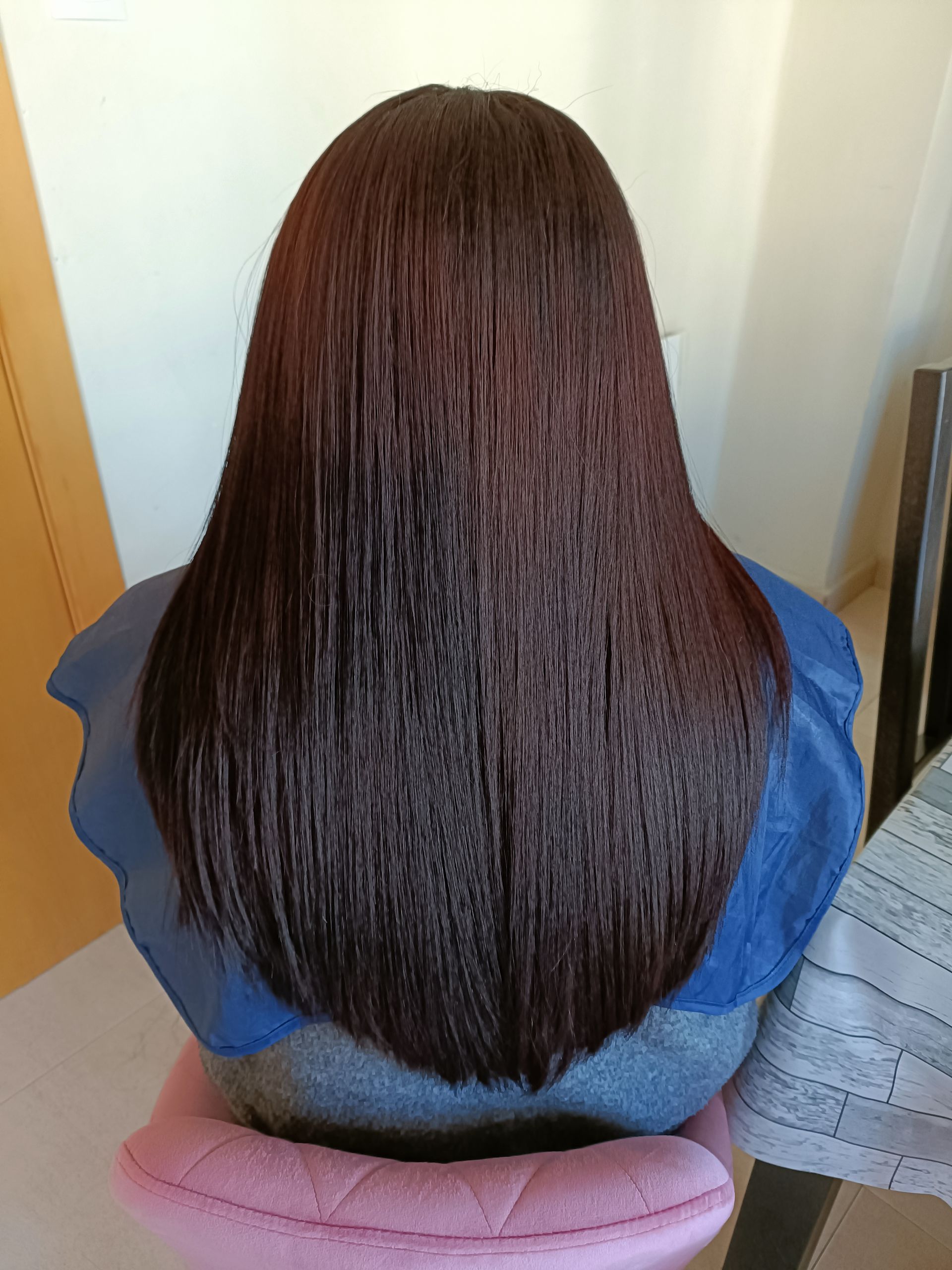 Una peluquera está peinando a una mujer en un salón de belleza. Al fondo se ven otros clientes, espejos