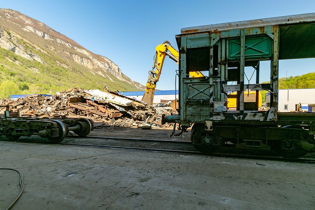 Terrain dans une recyclerie avec une excavatrice jaune à côté d'un tas de gravats et d'une remorque de camion ouverte sous un ciel dégagé