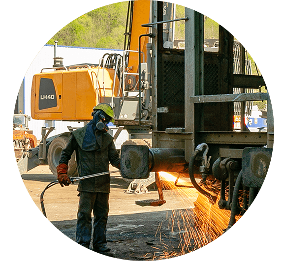 Un ouvrier utilise un chalumeau à côté d'engins de chantier, projetant des étincelles sur le chantier.