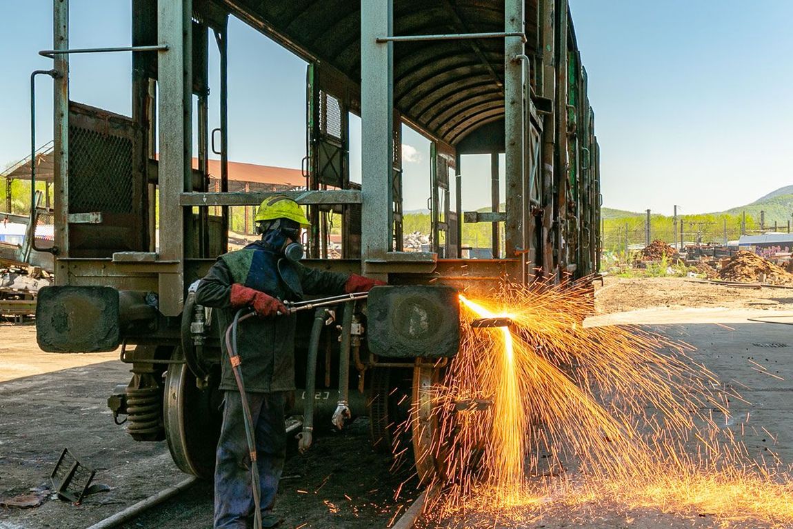 Un ouvrier découpe du métal sur le châssis d'un camion, des étincelles jaillissant dans un atelier en plein air.
