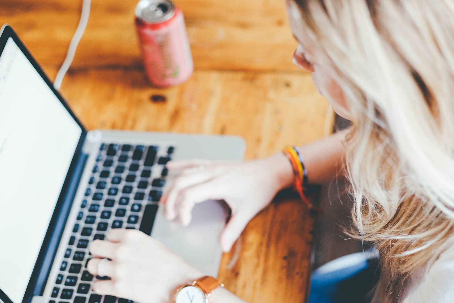 Una mujer está escribiendo en una computadora portátil sobre una mesa de madera.
