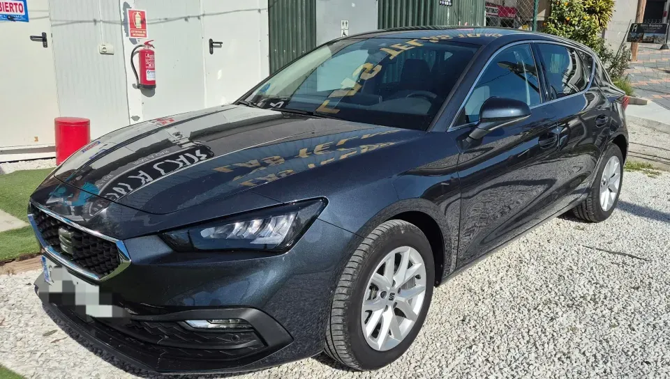 Un SEAT León de color gris oscuro aparcado en un terreno de grava cerca de un edificio con un extintor.