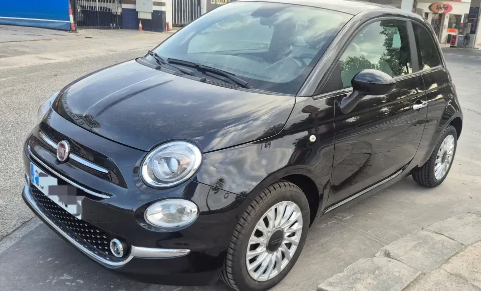 Un Fiat 500 hatchback de color negro brillante estacionado sobre una superficie de asfalto, visto desde un ángulo de tres cuartos frontal.