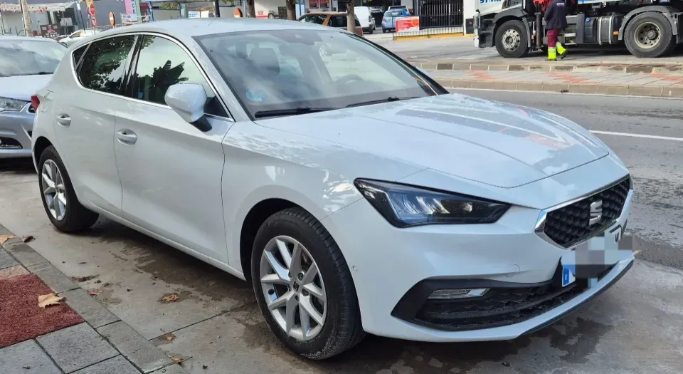 Un SEAT León hatchback blanco estacionado en una calle de la ciudad, visto desde un ángulo de tres cuartos frontal.
