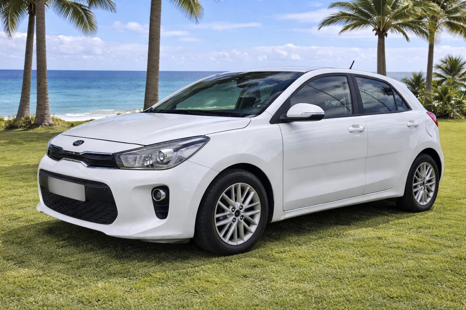 Un Kia Rio hatchback blanco estacionado en un césped con palmeras y el océano al fondo.