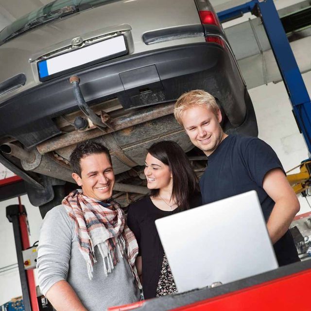 Un grupo de personas paradas debajo de un automóvil mirando una computadora portátil.
