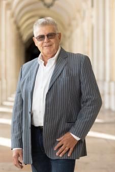 Un homme en blazer rayé et lunettes de soleil se tient dans une allée à colonnes.