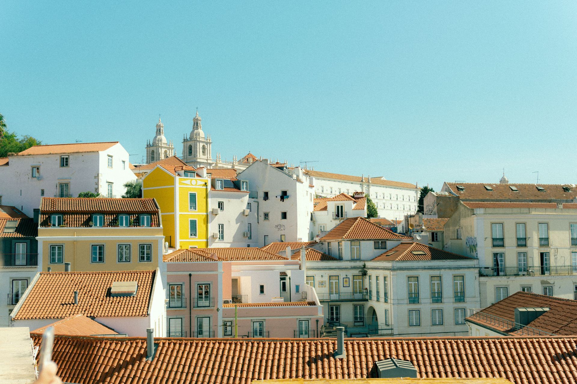 Village coloré à flanc de colline, avec ses bâtiments blancs et pastel et ses toits de tuiles rouges, sous un ciel d'un bleu limpide.
