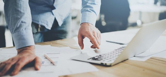 Un hombre está parado frente a una computadora portátil.