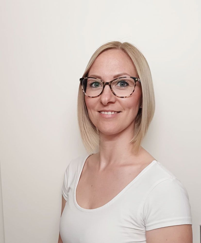 Eine Frau in einem blauen Hemd steht mit verschränkten Armen da und lächelt.