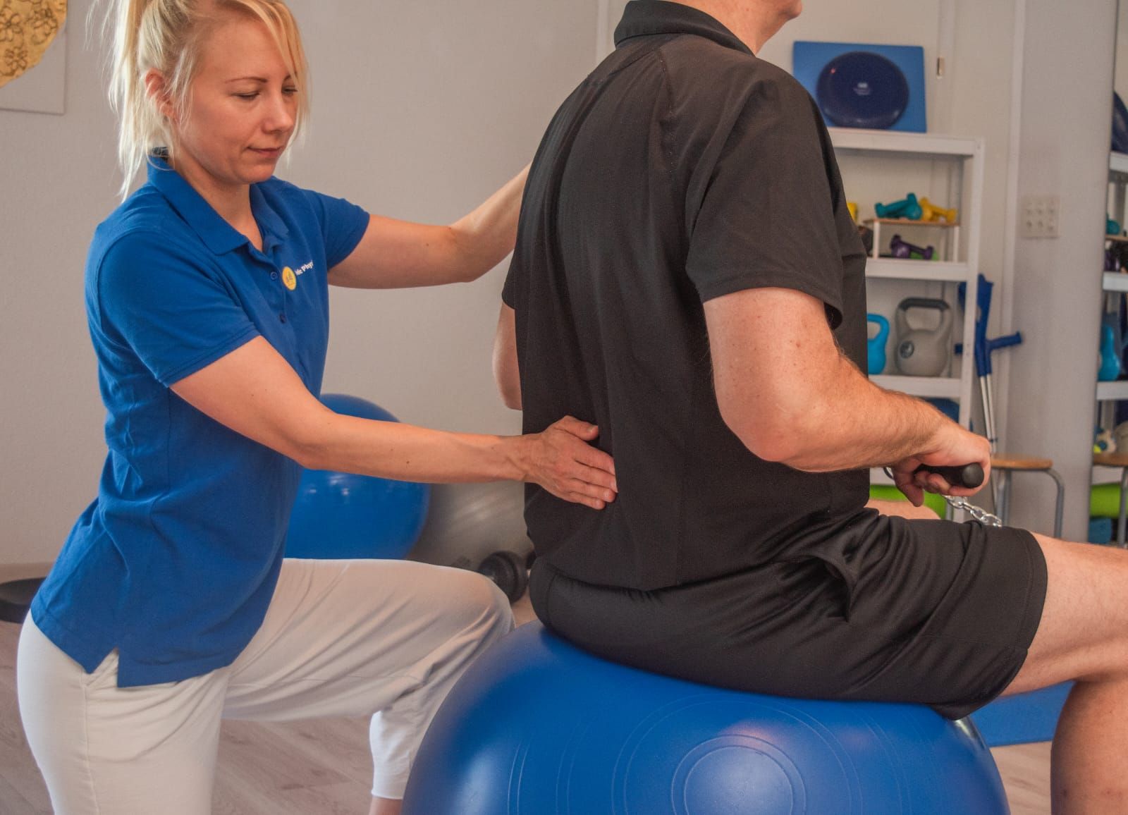 Eine Frau hilft einem Mann, sich auf einen blauen Gymnastikball zu setzen
